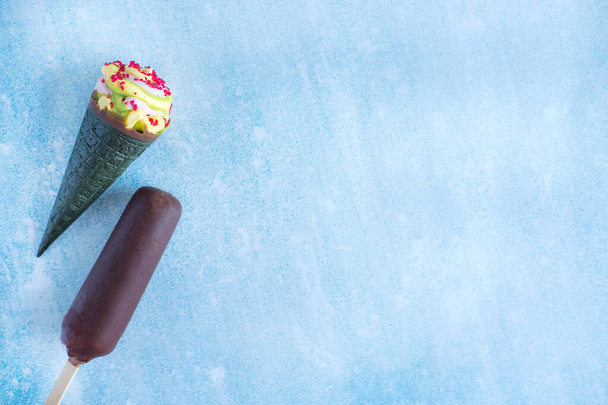 Jäätelöä suklaassa, jäätelötötterö vihreällä vohvelilla ja kirkkailla murusilla. Muutama jäätelö sinisellä taustalla näkymä ylhäältä
. - Valokuva, kuva