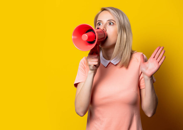 Blonde girl in pink dress with megaphone on yellow background - Фото, зображення