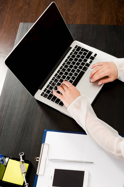 オフィスの敷地内のラップトップのキーボードに横たわっている女性の手のトリミングの垂直フレーム。リモートワーク、オンライン検索、情報検索の概念 - 写真・画像