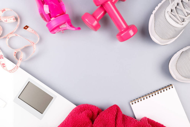 Fitness-Konzept flach auf grauem Hintergrund mit Turnschuhen, Notizblock, Waage, Klebeband, rosa Handtuch, Kurzhanteln und Wasserflasche, flacher Kopierraum vertikal - Foto, Bild