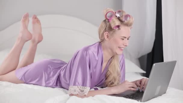 Blonde with a laptop and curled hair in a video call with parents from abroad. The quarantined girl communicates with friends or girlfriend while lying on a bed. Stay home concept. Prores 422 - Séquence, vidéo