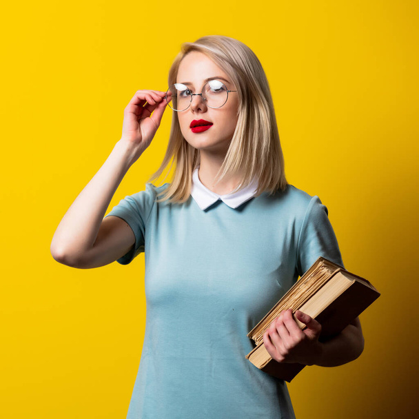 Blondes Mädchen in blauem Kleid und Brille mit Büchern auf gelbem Hintergrund - Foto, Bild