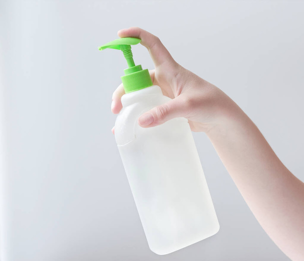 Młoda kobieta Ręcznie trzyma białą butelkę detergent do różnych powierzchni w kuchni, łazience i innych pokojach. Zbliżenie. Jasnoszare tło. koncepcja czyszczenia łazienki - Zdjęcie, obraz