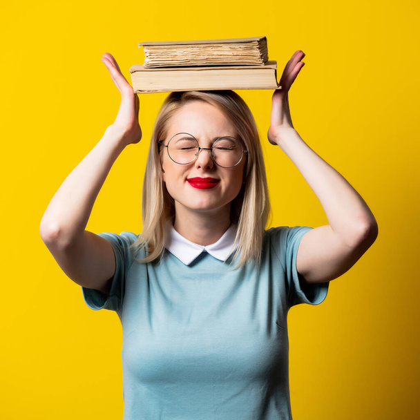 Sarışın kız mavi elbiseli ve sarı arka planda kitapları olan gözlüklü. - Fotoğraf, Görsel