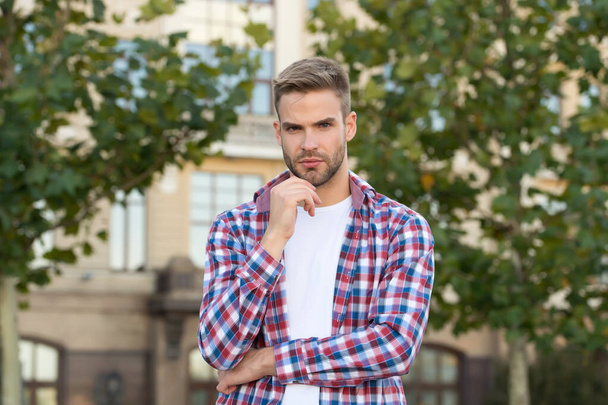 Spring fashion for men. Confident position. Good looking guy stand outdoors with crossed arms. Charismatic fashion model. Handsome unshaven man. Man wear checkered shirt. Male beauty and fashion - Foto, imagen