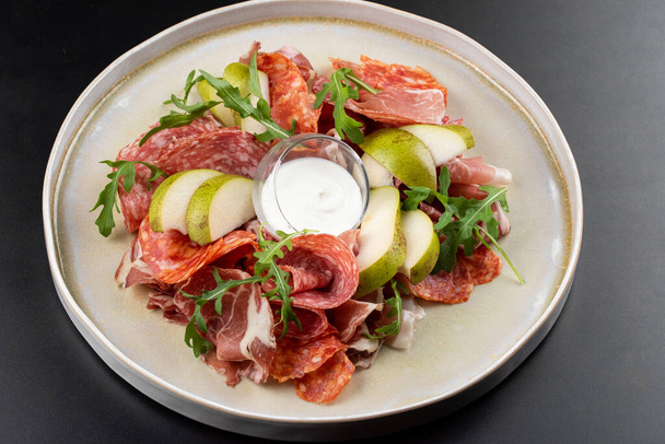 assiette de viande avec jamon et tranches de salami décorées avec poire et sauce sur fond de table
 - Photo, image