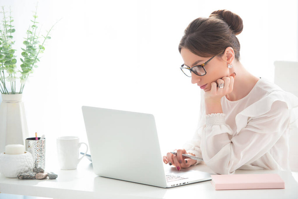 Молода жінка працює за столом з ноутбуком в офісі. Жіночий бізнес, віддалена робота
. - Фото, зображення