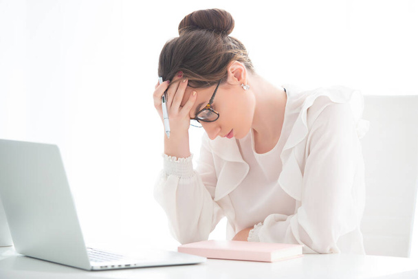 An upset young woman is sitting in an office at a laptop, and is holding her head in her hands. Problems at work. - Foto, Imagen