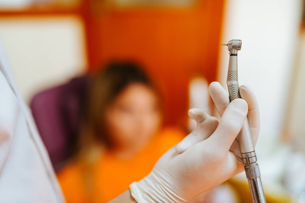 Feche a mão de um dentista caucasiano em uma luva segurando uma broca em um consultório de dentista
 - Foto, Imagem