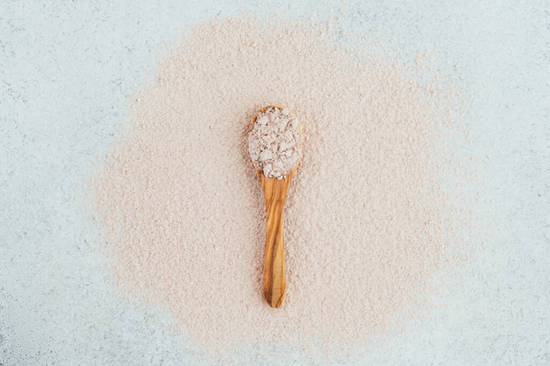 Pink clay in a wooden spoon on a pink, white background. - Фото, изображение