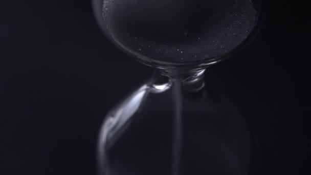 Sand in the hourglass on a black background in the dark. Time concept. - Footage, Video