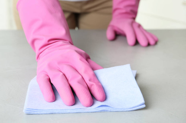 Woman in gloves wiping grey table with rag indoors, closeup - Φωτογραφία, εικόνα