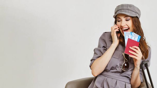 Een meisje in een grijze jurk spreekt aan de telefoon en heeft vliegtickets en een paspoort. Sluiten.. - Foto, afbeelding