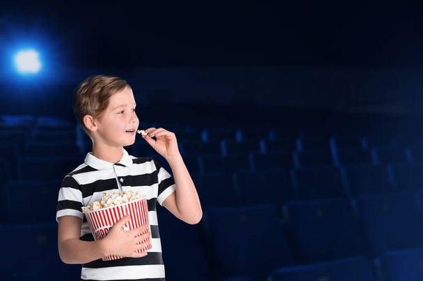 Cute boy with popcorn bucket in cinema, space for text - Fotó, kép
