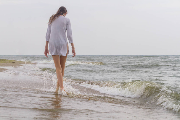 Beautiful young girl walking by the sea in white shirt and bare legs, Black Sea, Zatoka, Odesa, Ukraine - Fotó, kép