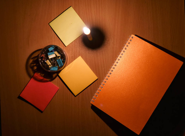 テーブルの上に置かれたノートと紙クリップのクローズアップ写真とキャンドルからのオレンジ色の光. - 写真・画像