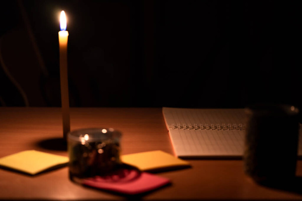 Fényképek az asztalra helyezett jegyzetfüzetekről és gemkapcsokról, gyertyák narancssárga fényével. - Fotó, kép