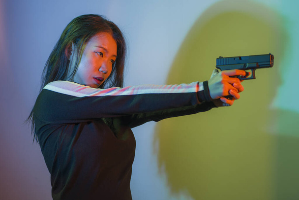 cinematic portrait of young attractive and dangerous special agent woman spy or Asian Korean mobster girl holding handgun pointing the gun fierce in Hollywood movie style - Foto, Bild