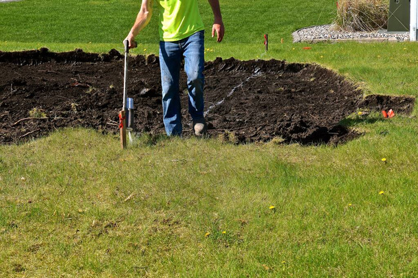 Um trabalhador de construção pulveriza uma linha branca para determinar os limites de uma base para a escavadeira
 - Foto, Imagem