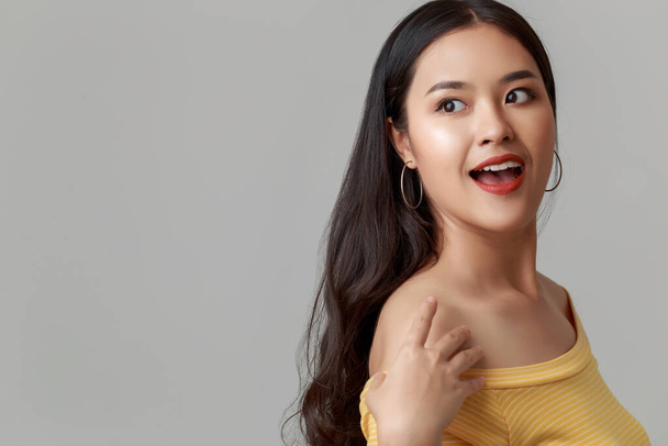 Close up young happy attractive Asian woman wearing yellow showing shoulder dress with sweet smiley face isolated on grey background. - Фото, зображення