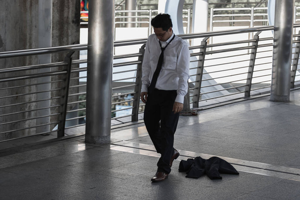 Unemployed stressed young Asian business man sitting on floor outdoors. Failure and layoff concept. - 写真・画像