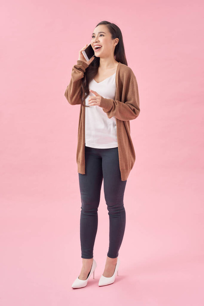 Full length portrait of a happy young woman talking on the phone isolated on a pinkbackground - Photo, Image