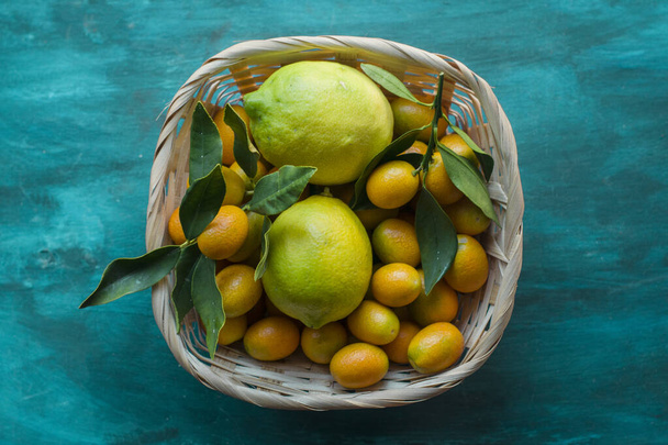 A basked full of kumquats and lemons on a light blue background. - Photo, Image