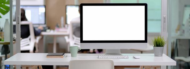 Close-up weergave van kantoor bureau met blanco scherm computer, mok en notebooks op wit bureau met witte stoel in glazen scheidingswand kantoor  - Foto, afbeelding