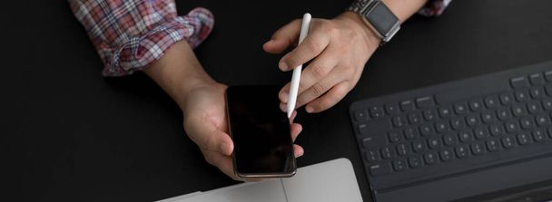 Fotografía aérea del hombre de negocios que usa el teléfono inteligente mientras trabaja con dispositivos digitales en la mesa de trabajo moderna oscura
 - Foto, Imagen