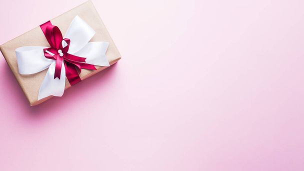 Gift or present box with a big bow on a pink table top view. Flatlay composition for Christmas birthday, mother day or wedding - Zdjęcie, obraz