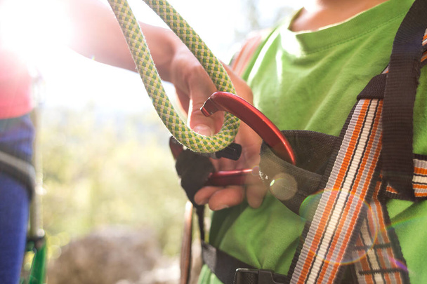 The instructor teaches the child to use climbing equipment, The boy is preparing to climb a rock, A woman shows a child how to use a carabiner for belaying, Mother ties the rope to the safety system. - Fotoğraf, Görsel