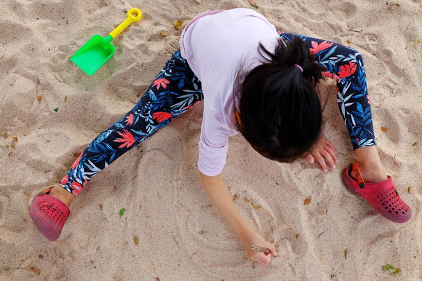 A cute Asian girl playing in a sandbox with colorful plastic toys.  - Foto, imagen