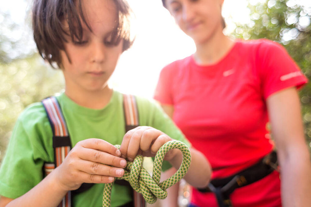 Un enfant apprend à tricoter le nœud de sécurité de la corde. Corde d'escalade pour l'assurage. Un petit garçon essaie de faire un nœud. Entraînement scout. Mains d'enfants et corde de sécurité. Enseigner aux enfants. - Photo, image