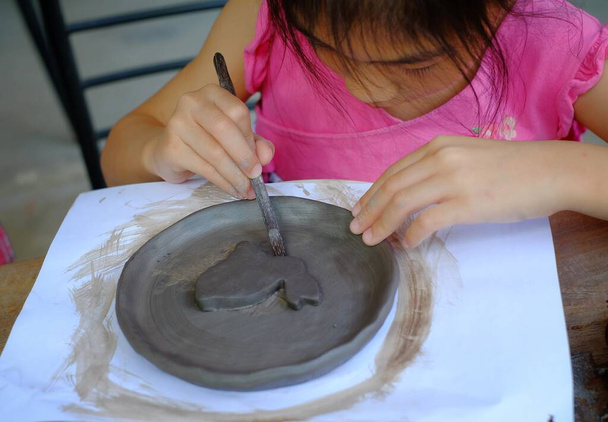 Une jolie fille asiatique dans une classe de poterie, faire un plat d'argile avec un motif de lapin au milieu
.  - Photo, image