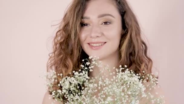 Retrato de una joven hermosa mujer sonriente con maquillaje con una larga mujer de pelo rizado marrón sosteniendo un ramo de flores blancas - Imágenes, Vídeo