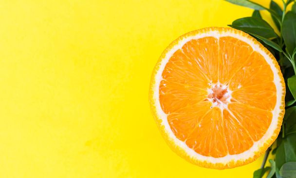 A half of orange and leaves. Creative summer concept. Food concept. Yellow background. Flat lay. - Foto, Imagen