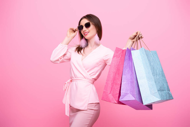 Fashionable elegant girl in sunglasses with multi-colored shopping bags is happy from discounts and sale. Isolated on pink background. - Foto, Bild