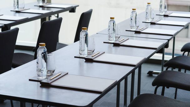 Garrafas de água de plástico, copos de beber com lápis e papel branco sobre a mesa preparada para seminário ou reunião de negócios na sala de conferências do hotel
 - Foto, Imagem