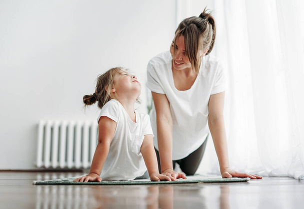 Happy mom and little daughter doing yoga morning exercise together at bright interior home - Foto, Bild
