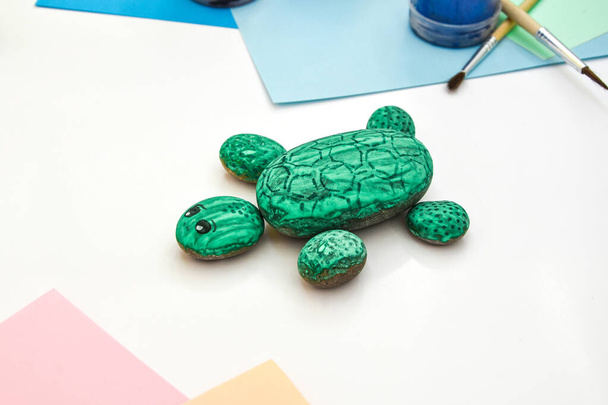 Een rotsgroene schildpad stap voor stap op een steen schilderen. Kinderen kunstproject. Doe-het-zelf concept. Stap voor stap foto instructie.Bekijk van bovenaf. Werken met kinderen en volwassenen in quarantaine. - Foto, afbeelding