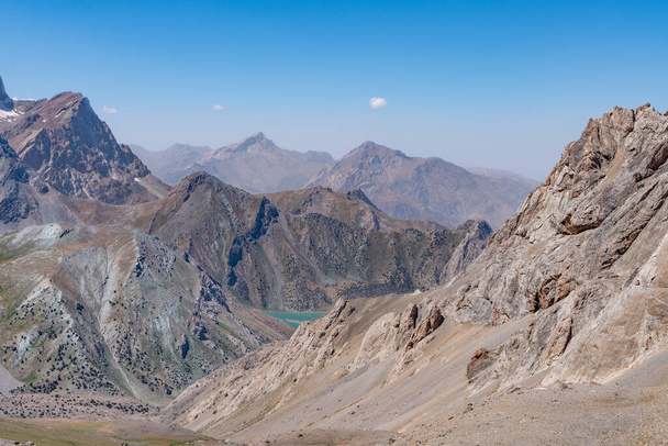 澄んだ青い空と岩場の丘を持つ美しい山のトレッキング道路とタジキスタンのファンマウンテンのオーディン湖の景色 - 写真・画像