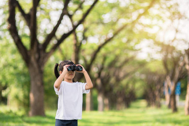 Happy child girl playing with binoculars. explore and adventure concept - 写真・画像
