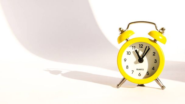 Yellow alarm clock on white background, copy space, Cute yellow metal alarm clock with large shadow on white paper background. Eleven o'clock - Foto, Imagen