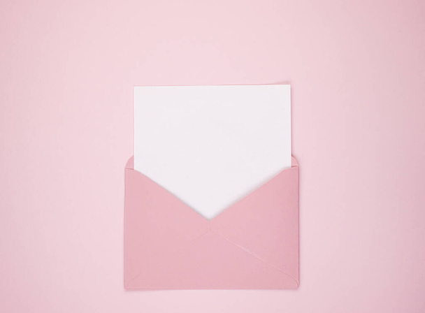 An open pink envelope containing a blank sheet of white paper, space for text. Space for text on a pink background. Concept of women's holidays and Valentine's Day. Flat lay - Foto, immagini