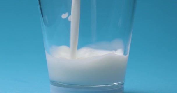 Milk is poured into a milk glass on a blue background. - Footage, Video