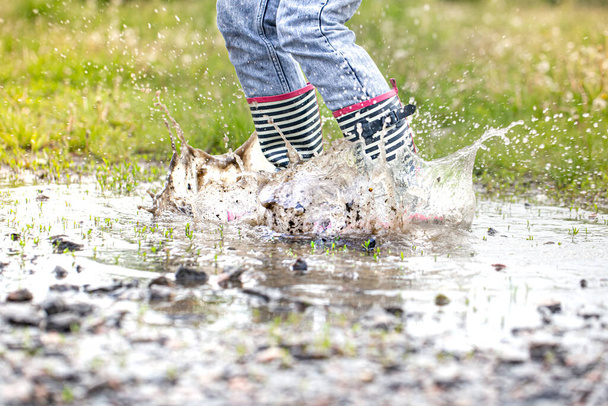 Ein Kind in Gummistiefeln springt in eine Pfütze. Aus nächster Nähe. Herbst-Sommer-Konzept - Foto, Bild
