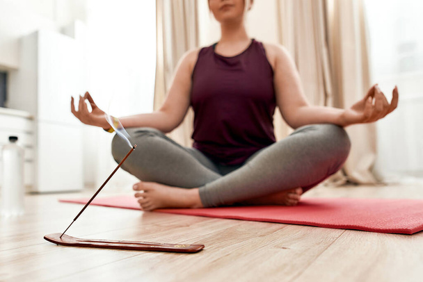 Revive your spirit. Cropped shot of young curvy woman in sportswear burning incense while sitting in the lotus position on a yoga mat at home - Фото, зображення