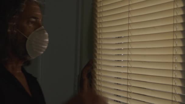 koronavírus, férfi orvosi maszkot visel, elszigetelten, kinézve az ablakredőnyön. - Felvétel, videó