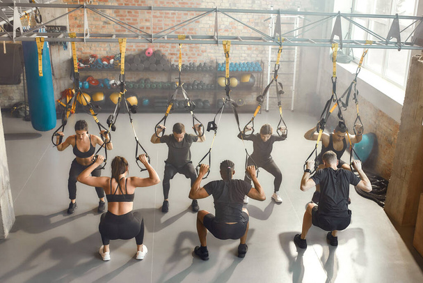 The Training Space. Group of sportive people doing fitness TRX training exercises at industrial gym. Push-up, group workout concept - Valokuva, kuva