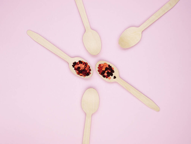 Eco-friendly biodegradable compostable wooden spoons on a soft pink background. Red confetti hearts on spoons. Background for the holidays - 写真・画像